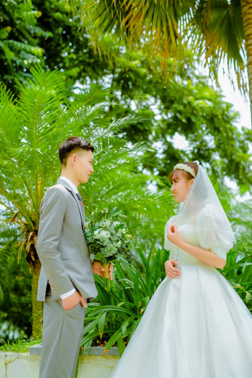 man and woman in wedding dress standing under green tree